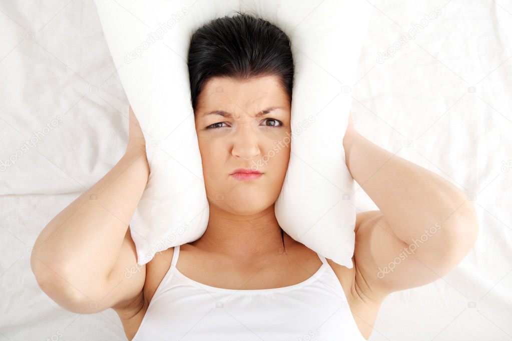 Female lying on bed and closing her ears with pillow. Insomnia