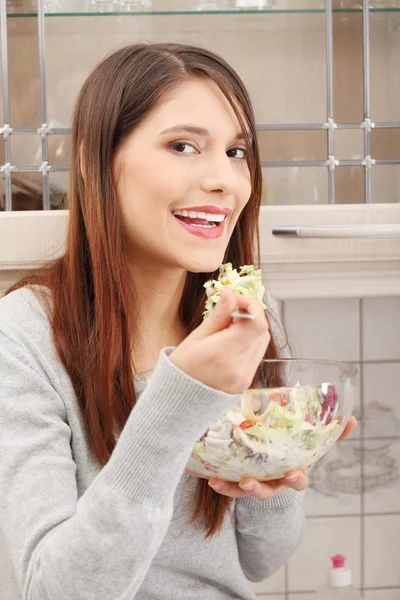美丽的女人在厨房里吃沙拉 — 图库照片