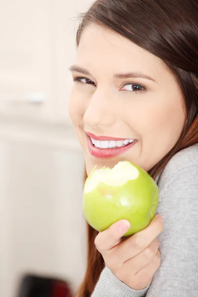 Woman in kitchen eating green apple — Stock Photo, Image