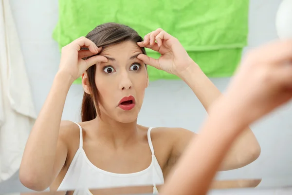 Schockierte junge Frau überprüft ihre Falten — Stockfoto