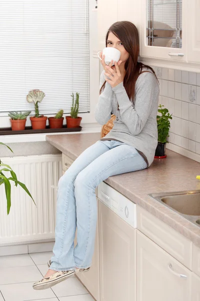 Молода жінка має каву або чай на кухні — стокове фото