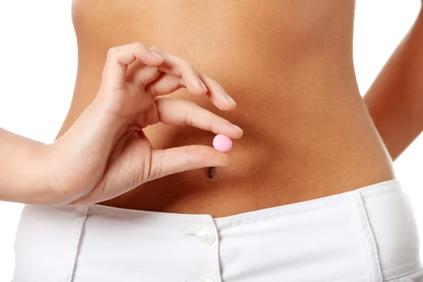Frau hält rosa Pille gegen ihren nackten Bauch. — Stockfoto