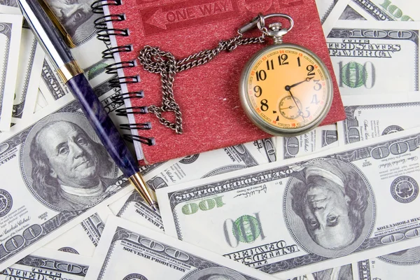 Lommeklokke, notatbok og penn på en stabel med dollar – stockfoto