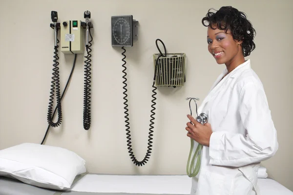 一个漂亮的黑色女医生在考试办公室拿着听诊器的实验室外套 — 图库照片