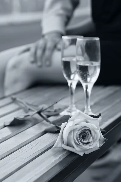 Rose and two wineglasses with champagne on the bench in black and white with soft blue tint