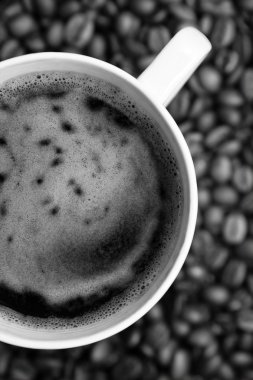 Coffee cup over coffee beans in black and white tones clipart