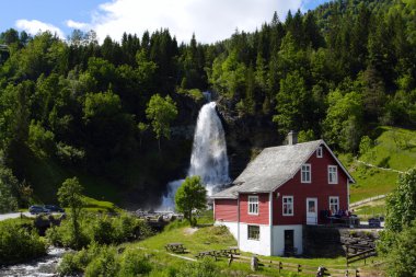 Traditional norwegian wooden house with waterfall in the distance clipart