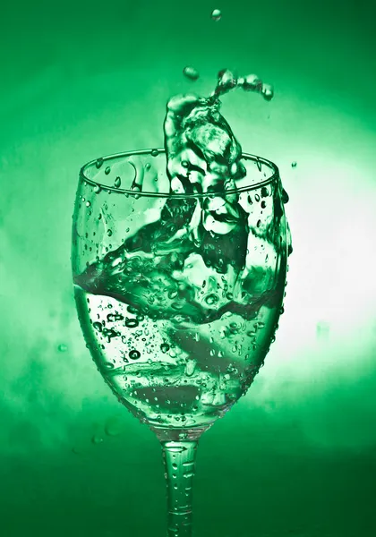 Glass with splash on green background — Stock Photo, Image