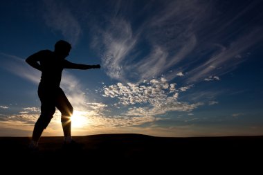 The silhouette of the guy against a decline, the beautiful sky, is engaged in martial arts clipart