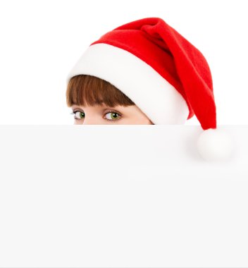 Green-eyed woman in Santa red hat peeking over blank billboard clipart