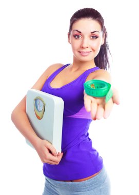 Beautiful young woman wearing sports clothes holding scales and a measuring tape (focus on the woman) clipart