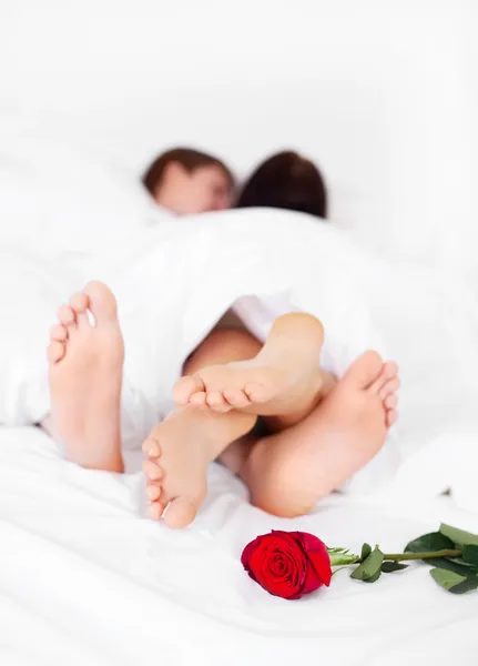 花にフォーカスがベッドに横たわっているバラと自宅のベッドの上の若いカップルのフィート — ストック写真