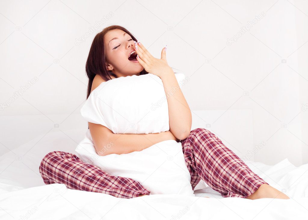 Beautiful young woman sitting on the bed and yawning
