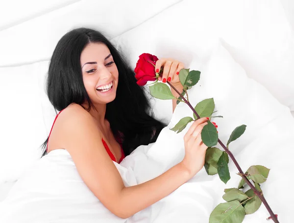 美丽的黑发女人醒来并在她的床上发现一朵玫瑰 — 图库照片