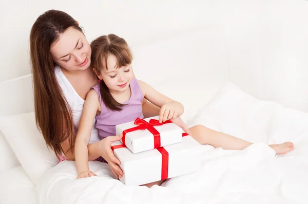 Beautiful young mother and her five year old daughter opening presents on the bed at home