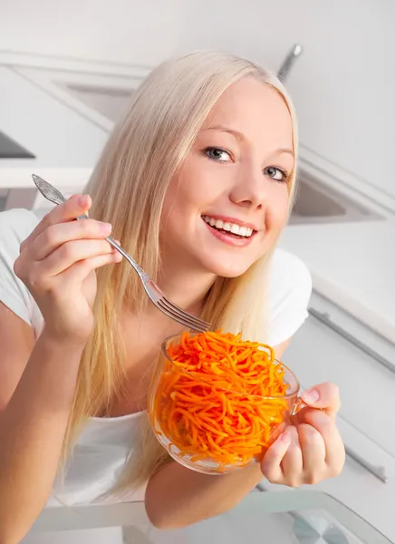 美丽的年轻女子在家里的厨房里吃胡萝卜沙拉 — 图库照片