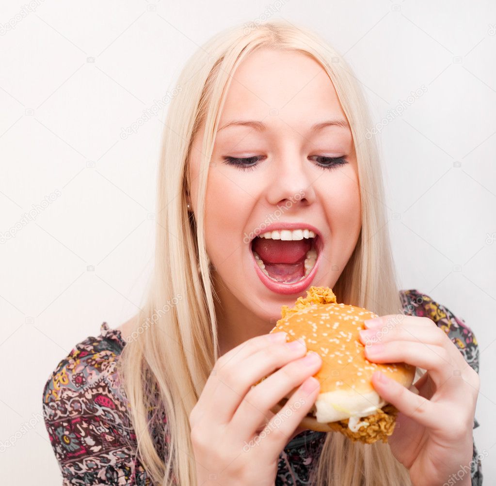 Happy young woman eating a hamburger with chicken, isolated against white background