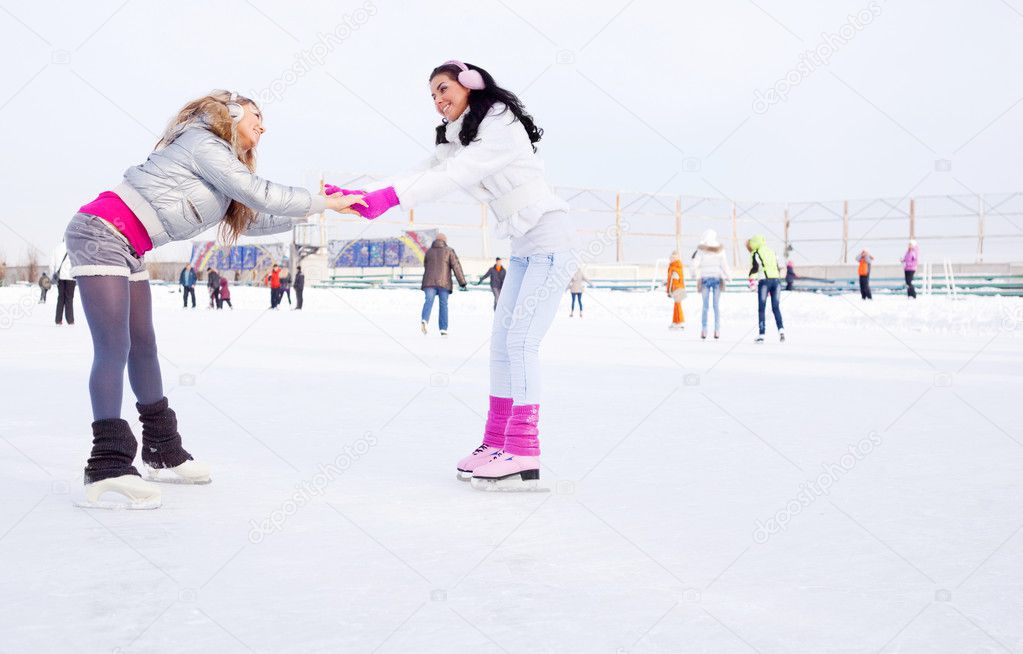Two beautiful girls ice skating outdoor on a warm winter day