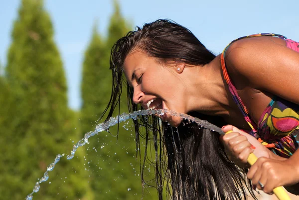Молодая девушка пьет воду из шланга — стоковое фото