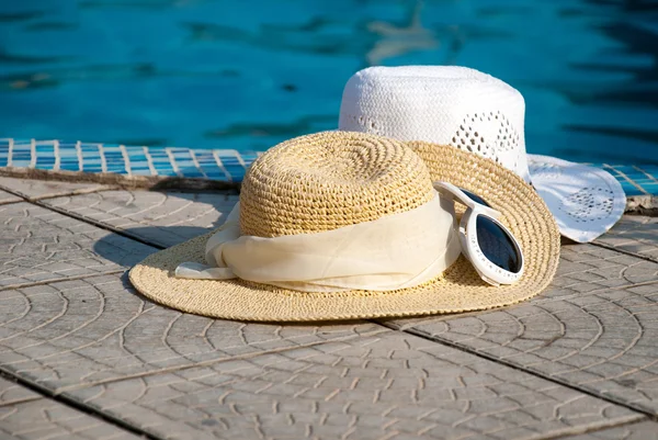 Солом'яні шапки і сонцезахисні окуляри лежать на межі басейну — стокове фото