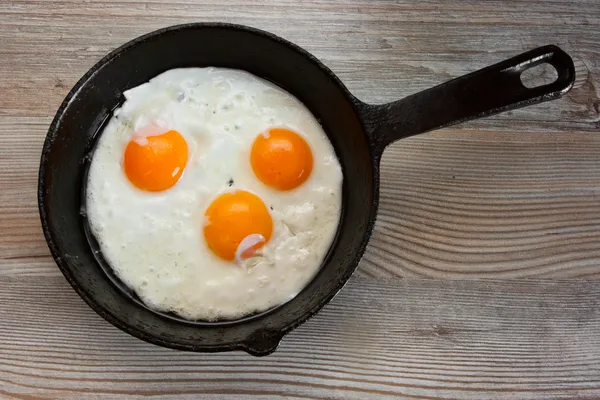 Trzy smażone jajka w patelni na stole — Zdjęcie stockowe