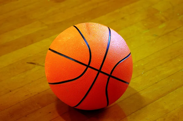 在聚光灯下休息的硬木地板上的篮球 — 图库照片
