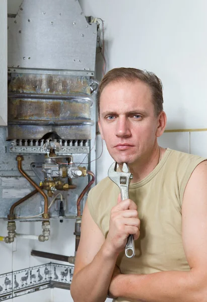 El hombre con una llave inglesa piensa en la reparación de un calentador de agua a gas — Foto de Stock