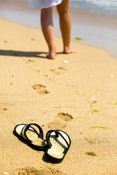 Zapatillas de playa sobre arena y pies femeninos sobre un fondo fuera de foco —  Fotos de Stock