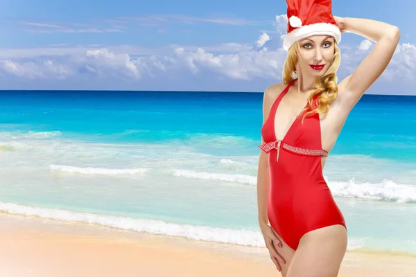The girl in a bathing suit and a cap of Santa Claus and ocean on a backgrou — Stock Photo, Image