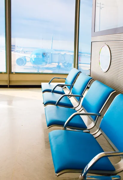 Empty armchairs in hall of expectation of airport and plane behind window