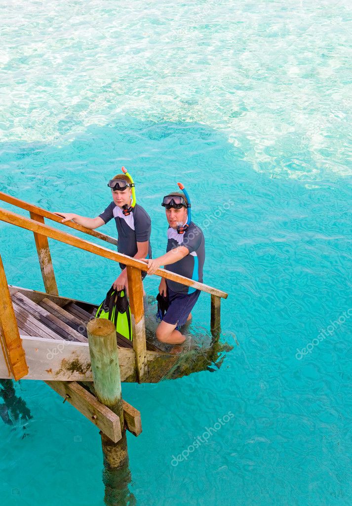 Two persons with the equipment for a snorkeling at steps at ocean. Maldives.