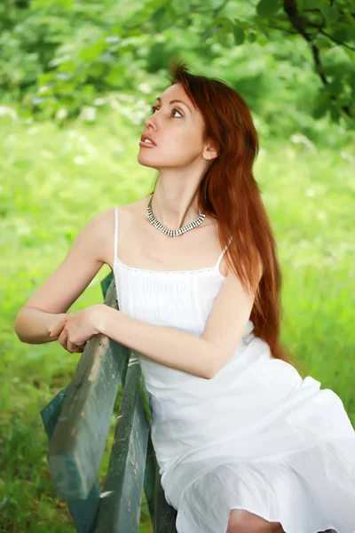 The beautiful girl on a bench in a garden — Stock Photo, Image