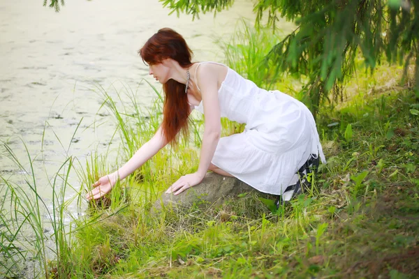 stock image The beautiful girl in a white sundress on the bank of wood lake