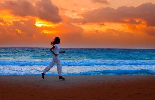 Силует жінки, біжить на заході сонця уздовж океанського узбережжя — стокове фото
