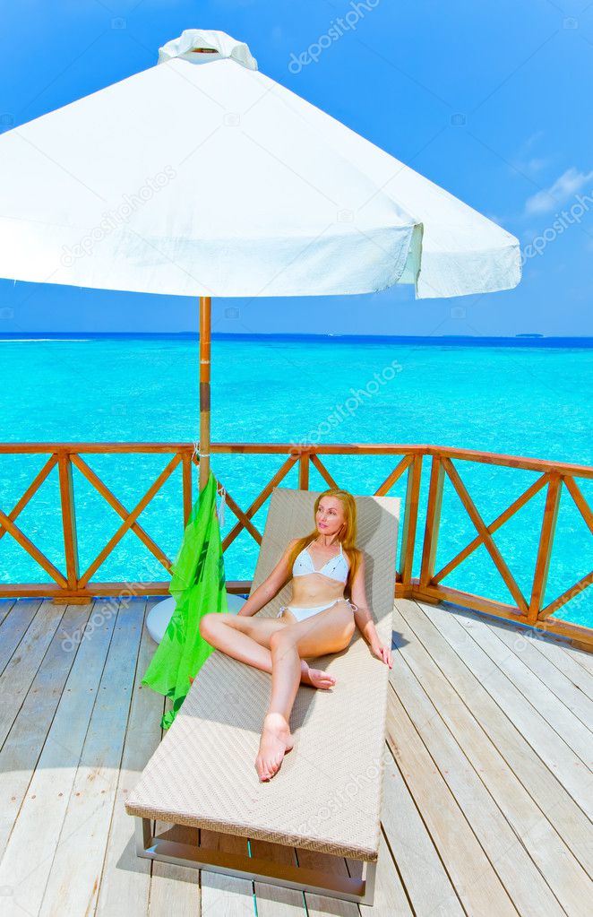 Young woman tans on a terrace of water villa on ocean Maldives