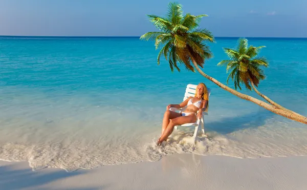 Het meisje in een chaise lounge op oceaan onder palmbomen op een zonsondergang — Stockfoto