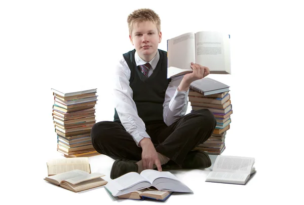 O estudante em um uniforme escolar senta-se em um soalho, perto de pacotes de livros , — Fotografia de Stock