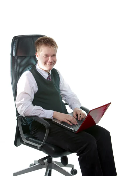 Счастливый школьник в офисном кресле, с ноутбуком — стоковое фото