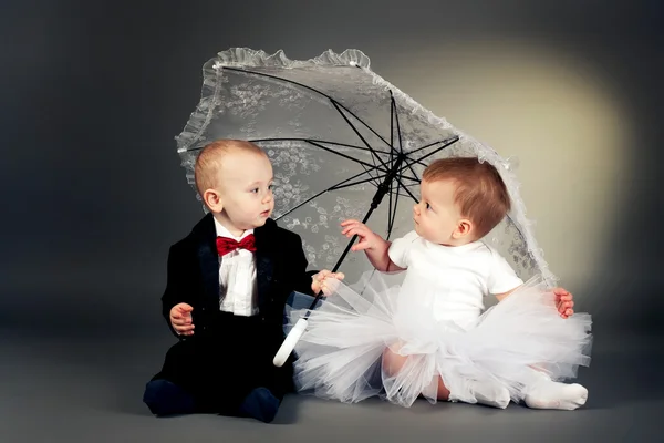 Kleine jongen en meisje zitten onder de paraplu Stockfoto