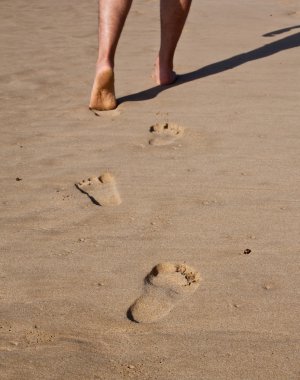 Footprints in wet sand in a line with a man walking on the beach clipart