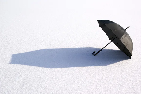 stock image Black large umbrella lies on snow in sun