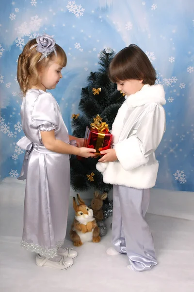 Leuk meisje en een jongen in de buurt van een kerstboom met cadeau in de hand — Stockfoto
