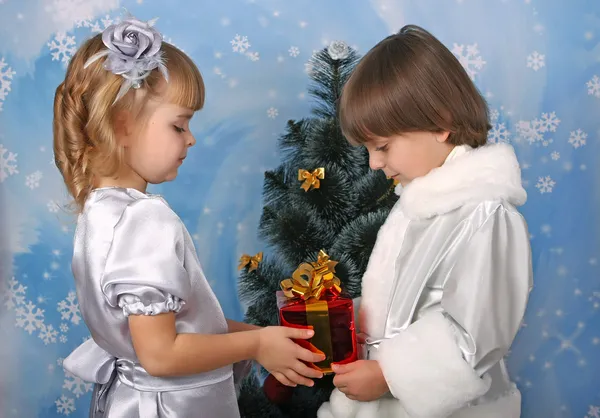 Linda chica y un niño cerca de un árbol de Navidad con regalo en la mano — Foto de Stock