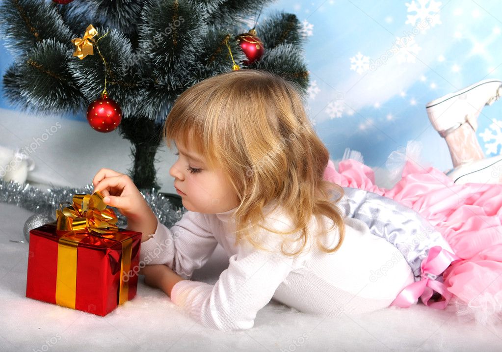 Beautiful girl with a gift lies near the Christmas tree