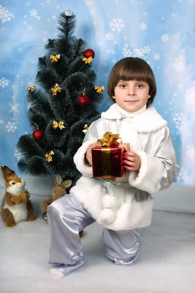 Хлопчик біля ялинки з подарунком в руці — стокове фото
