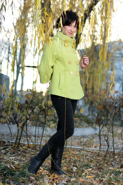 Beautiful girl in the green coat in the branches of willow autum — Stock Photo, Image