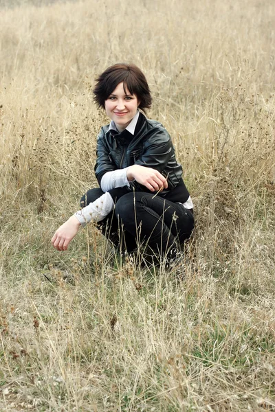 Девушка, сидящая в поле сухой травы улыбаясь — стоковое фото