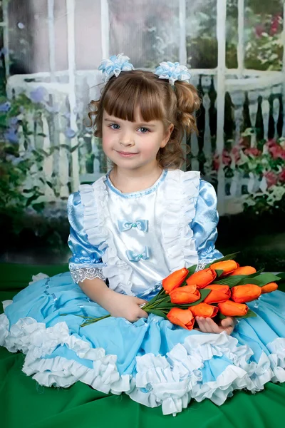 Krásná dívka v modrých šatech se posadil s červenými tulipány — Stock fotografie
