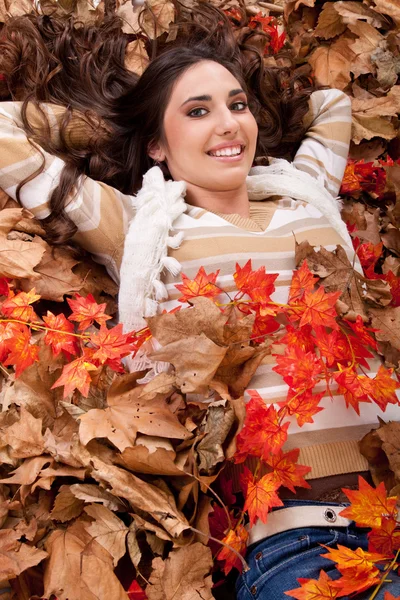 Jolie fille brune dans des feuilles d'automne sèches — Photo