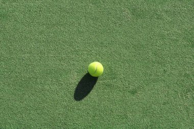 Tennis ball on a green artificial court surface,natural lighting and shadows. clipart